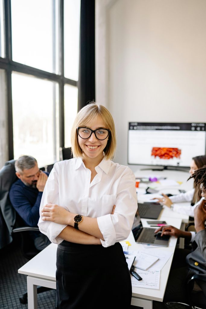 pexels-photo-7793712-7793712 Professional businesswoman smiling in office setting with colleagues working in the background.